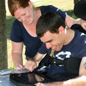 Gord, a smiling gentleman we support, with his support worker using his iPad as a communication device 