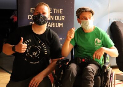 image shows two gentlemen with thumbs up - a person in a wheelchair supported by PHSS with the Astronomy in Action partner in front of the planetarium dome
